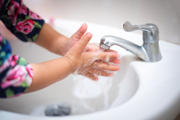 Sweet Asian child little girl washes her hands in bathroom