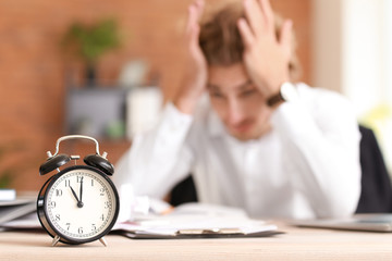 Alarm clock on table of stressed businessman missing deadlines