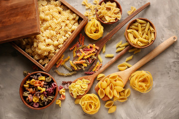 Different types of raw pasta on grey background