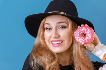 Beautiful young woman with tasty donut on color background