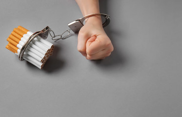 Woman handcuffed to cigarettes on grey background. Concept of addiction