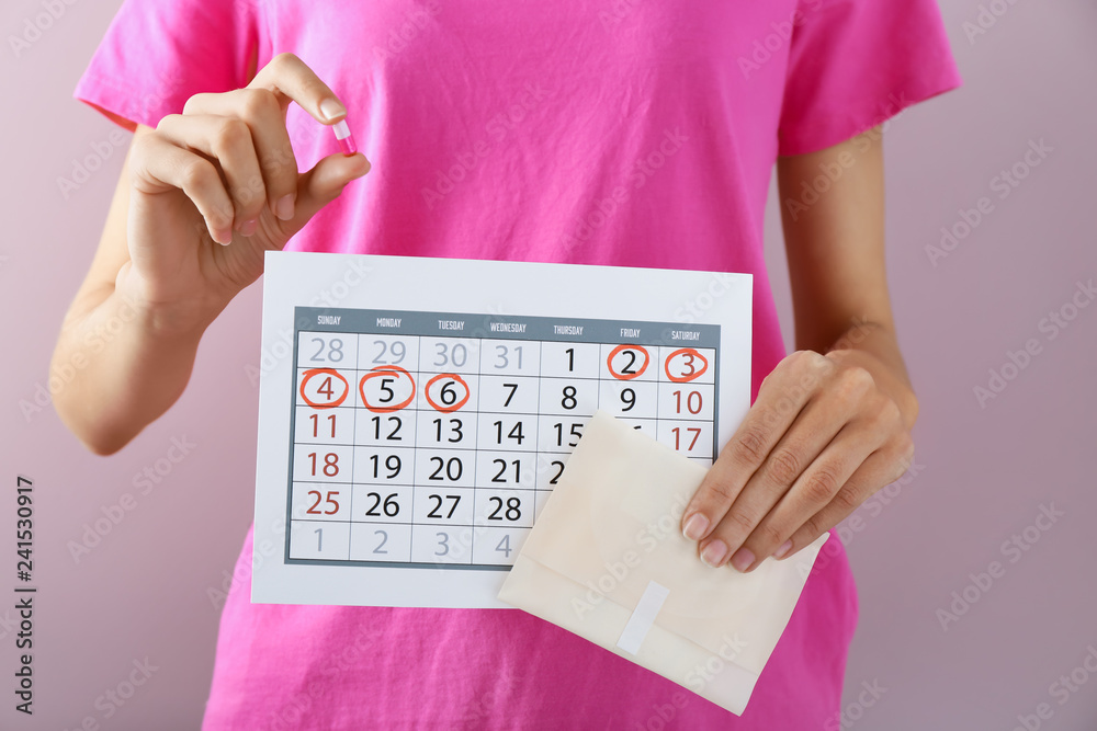 Wall mural Woman with menstrual pad, pill and calendar on color background