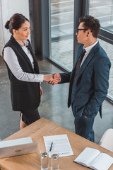 high angle view of young asian business people shaking hands, contract and laptop on table