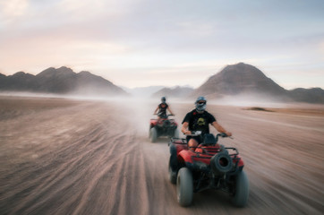 Buggy and ATV quads races in Sinai desert at sunset. Egyptian landscape with off-road vehicles and dust dirt road. Sharm el Sheikh, Egypt. Defocused motion blur - obrazy, fototapety, plakaty