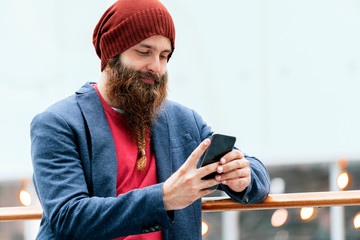 Stylish bearded man using phone indoors