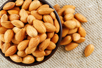 Almonds in a wooden cup on a burlap cloth background.