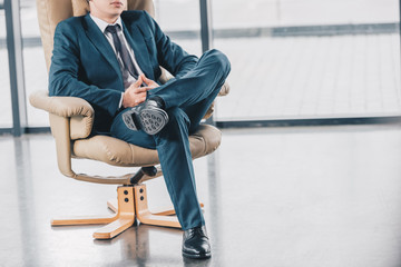 cropped shot of young businessman in suit sitting in chair at workplace