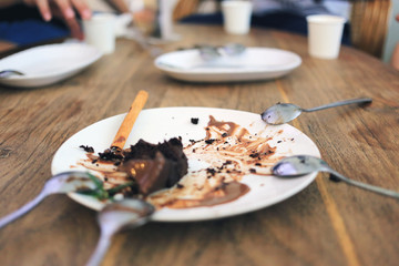 Finished eating chocolate cake in white dish. Dirty  food dish on wood table.