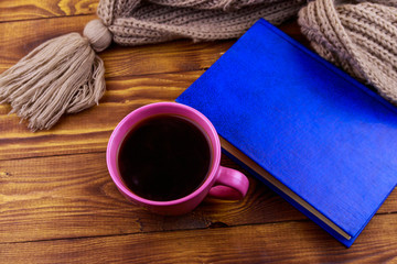 Cup of coffee, knitted scarf and book on wooden background
