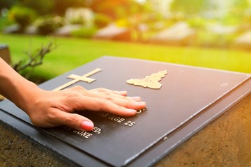 Woman's hand touching the black stone grave at cemetery with orange sunlight flare - Reminisce, Memory, miss, sad and lose person in the family or important people concept