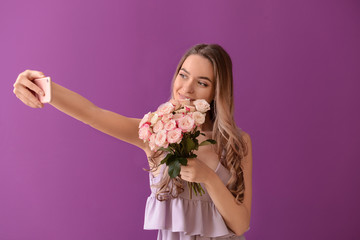 Beautiful young woman with bouquet of flowers taking selfie on color background