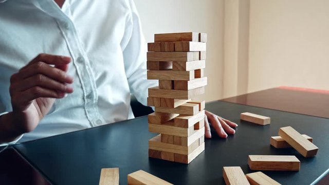 Business woman hand pull out a wooden block tower collapsing.