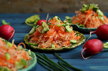 Carrot salad with cucumber and radishes on a plate on a blue wooden background