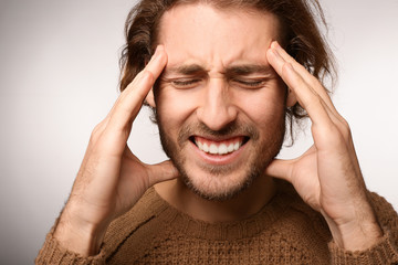 Young man suffering from headache on light background