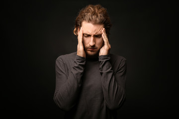Young man suffering from headache on dark background