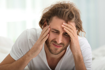 Young man suffering from headache in bedroom