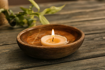 Fototapeta na wymiar Bowl with water and burning candle on wooden table in spa salon