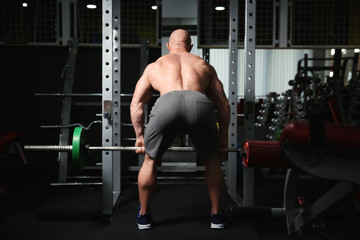 Fototapeta na wymiar Muscular man training with barbell in gym