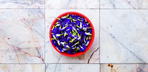 Fresh or Organic purple or pea flowers in red bowl putting on the marble floor background - Herb food, Nature and Plant growth concept: Scientific name of flower: Clitoria ternatea L.)  