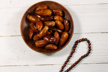 Dates fruit and rosary on white wooden table. Top view