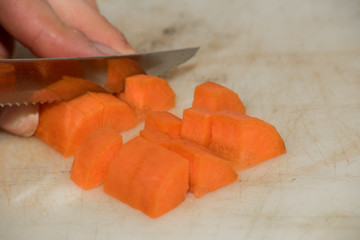 Female hand cuts a carrot with a metal knife on a plastic board