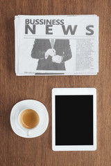 top view of cup of coffee, tablet with blank screen and business newspaper on wooden tabletop