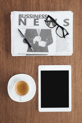 elevated view of cup of coffee, tablet with blank screen and business newspaper on wooden tabletop