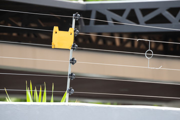 high voltage security fence on house wall with blank yellow plastice sign.