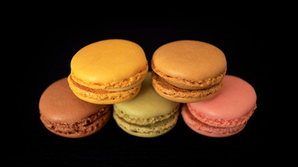 Assortment of traditional French macaroons or macarons, selection of different colors and flavors, very light bite-size confectionery, stacked and isolated against black background and selective focus