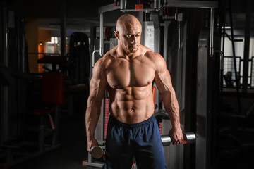 Fototapeta na wymiar Muscular man training with dumbbells in gym