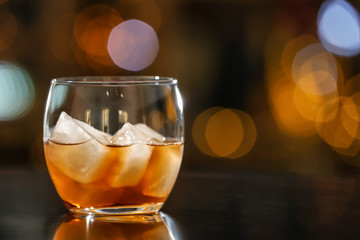 Glass of whiskey with ice on table in bar