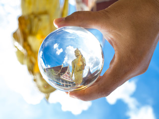 Gold Buddha statue standing image in a crystal glass ball holding on left hand in a cloudy day.