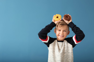 Naklejka premium Cute little boy with donuts on color background