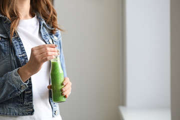 Woman with bottle of tasty smoothie indoors