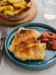 Fried fish with tomato-olive sauce and potatoes.