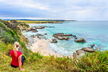 Female sitting by the coastal bluff looking out to the rocky beach belo