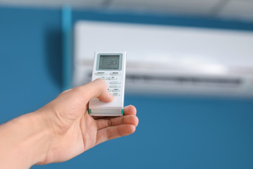 Young man switching on air conditioner indoors, closeup