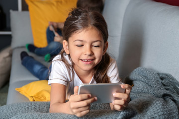 Cute little girl playing with smartphone at home