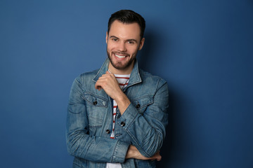 Fashionable young man in jeans jacket on color background