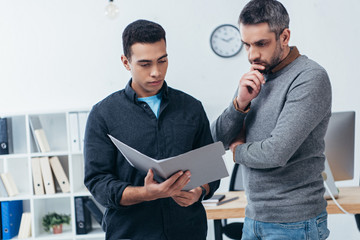 concentrated businessmen holding folder with papers and discussing project in office
