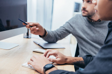 cropped shot of coworkers typing on keyboard and pointing at screen while working with desktop computer together