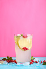 Glass of fresh lemonade on table against color background