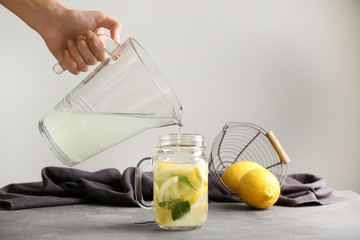 Woman pouring fresh lemonade into mason jar on table