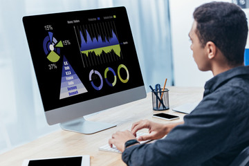 young businessman using desktop computer with business charts on screen in office