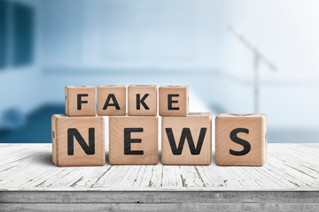 Fake news sign on a wooden desk in a blue room
