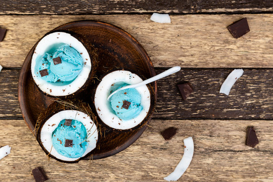 Blue ice cream with chocolate in coconut bowl on wooden background.