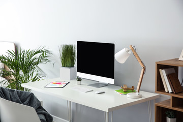 Stylish workplace with modern computer near light wall