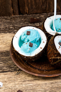 Blue ice cream with chocolate in coconut bowl on wooden background.