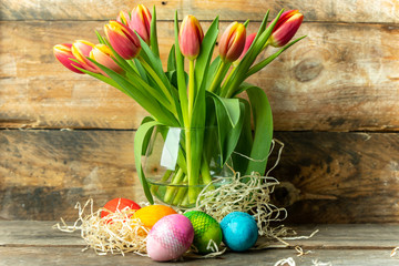 Easter eggs and spring yellow-orange tulips on a raw, rustic, wooden background
