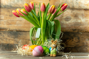 Easter eggs, bunny and spring yellow-orange tulips on a raw, rustic, wooden background